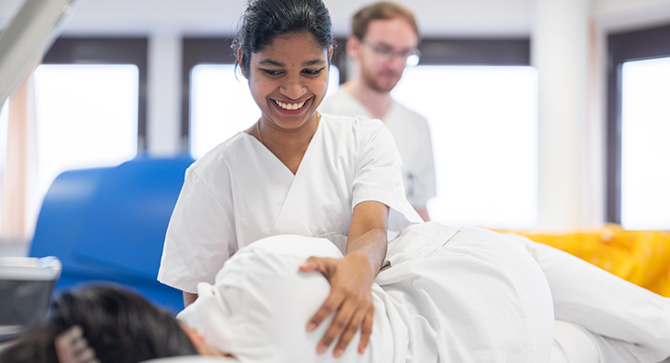 Pflegeschülerin führt unter Anleitung eine fachgerechte Lagerung einer Patientin durch.
